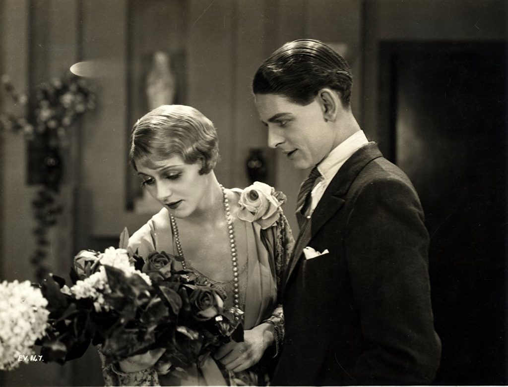 A glamorously-dressed Isabel Jeans and Robin Irvine in Easy Virtue (1927, dir. Alfred Hitchcock). She admires a bunch of flowers while he admires her, with lust.